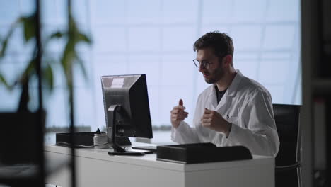 Tilt-down-shot-of-male-doctor-in-lab-coat-and-glasses-typing-on-laptop-while-working-at-desk-in-medical-office